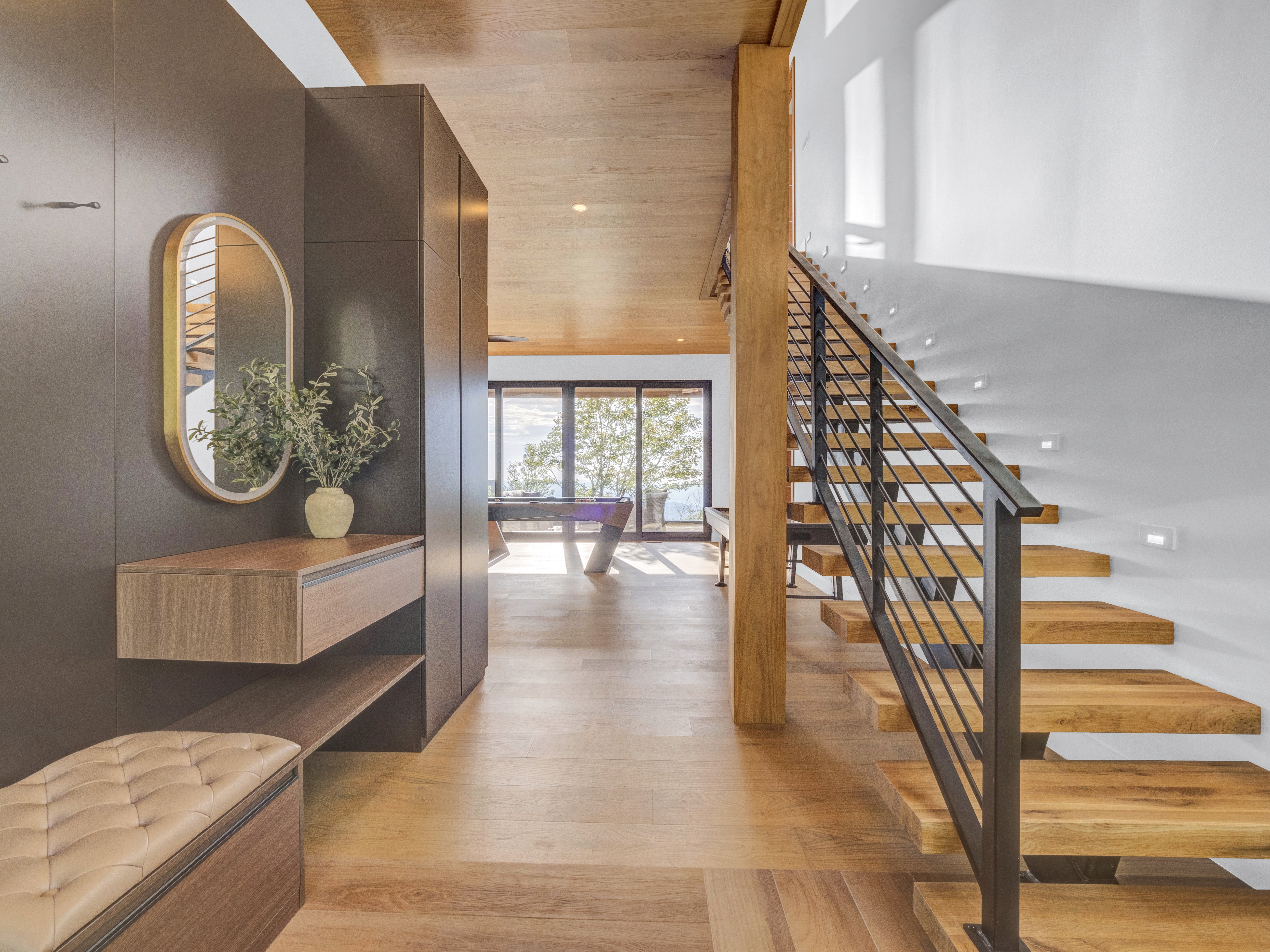 View from the foyer showing a custom floating wood staircase with black metal railings and a built-in bench leading to the game room