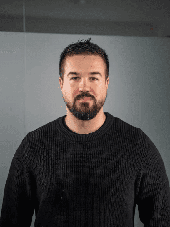 Man in glasses wearing a grey suit and blue tie, looking calmly at the camera.