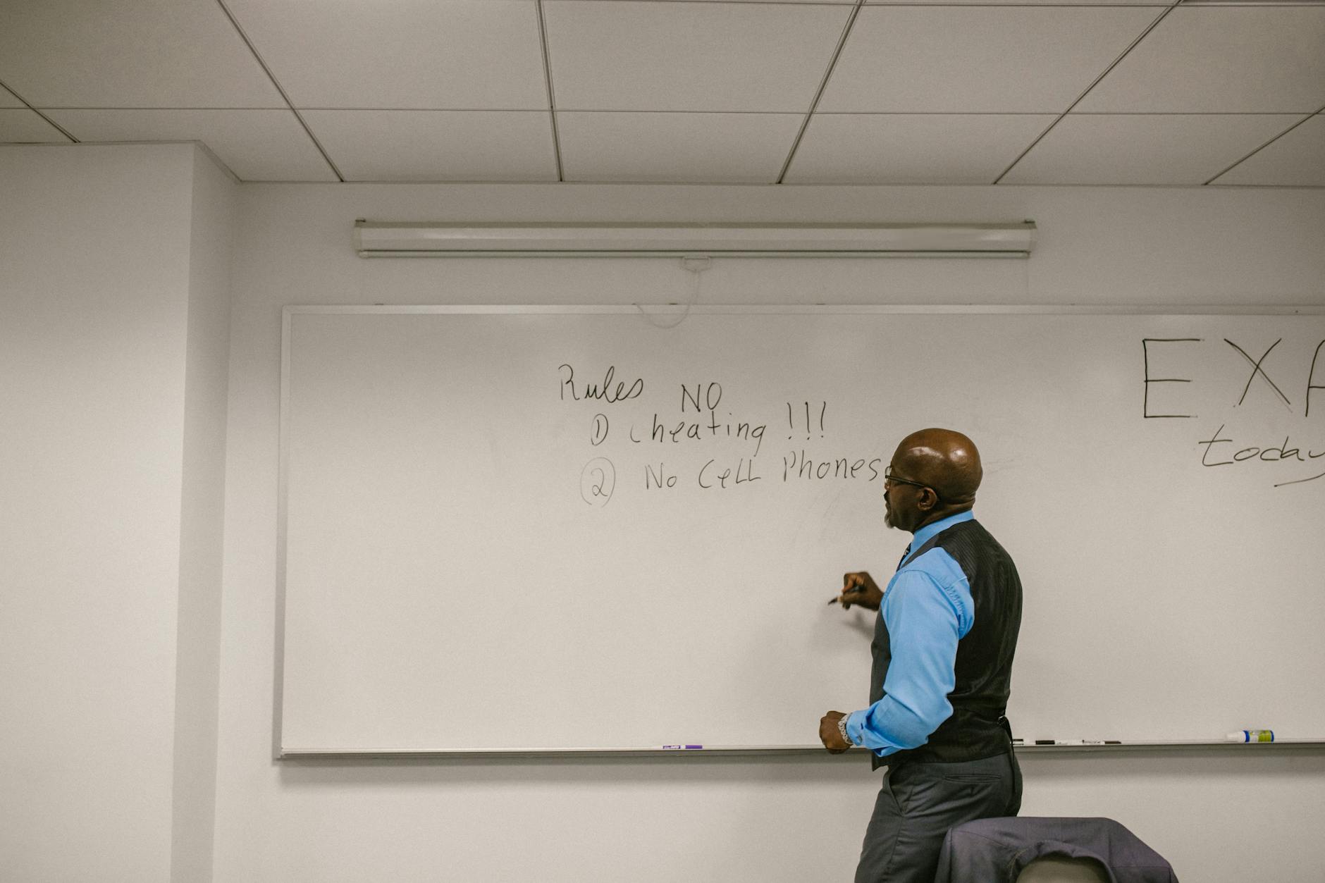 A teacher pointing to a list of classroom management strategies written clearly on a white chalkboard.