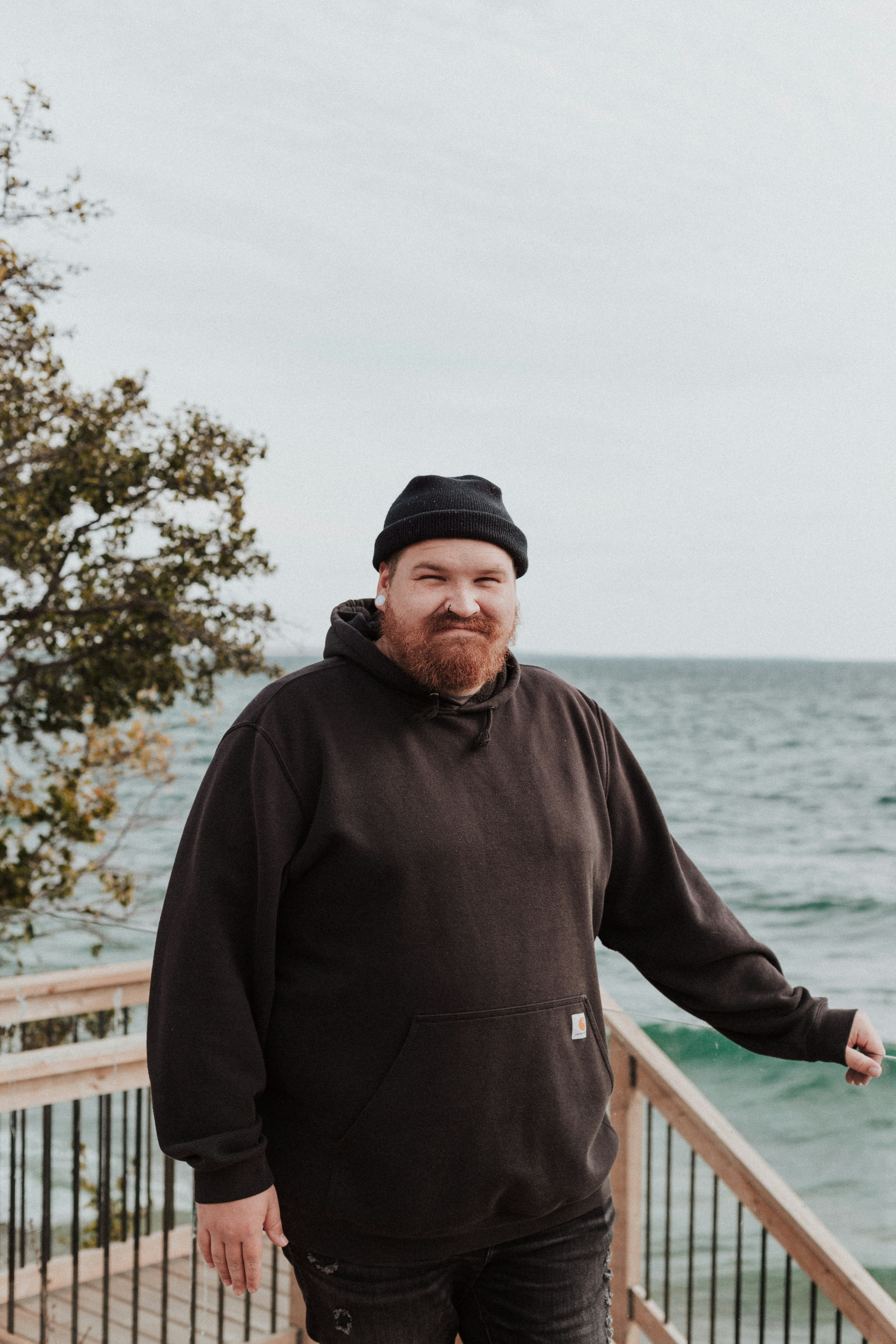 A man in a black hoodie standing on a wooden deck next to the ocean