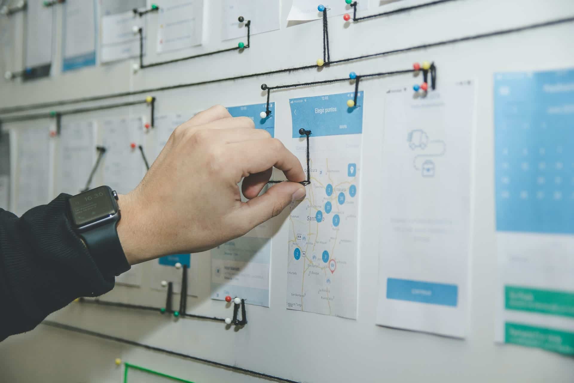 Hand organizing project planning documents on board with pins and strings.