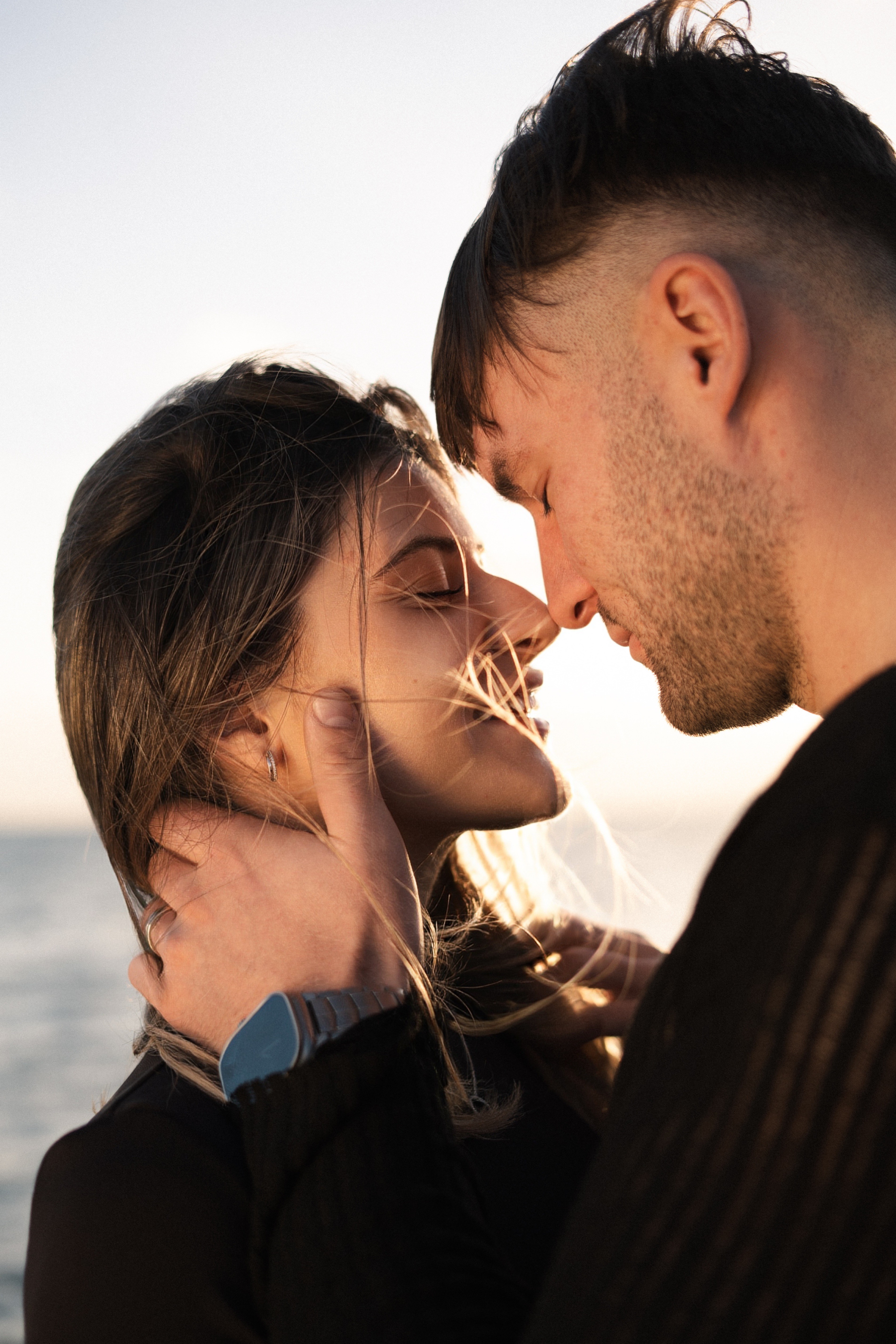 A couple sits closely on a rocky landscape with long grasses.