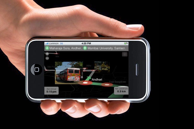 A hand holds a smartphone displaying a map application. The map shows a red bus labeled "Andheri" traveling along a green route marked with red dots. The time displayed on the phone is 4:20 PM, and the location is shown as Maharaja Sura, Andheri, Mumbai University, and Santacurr. The map also indicates the bus's route and destination. The phone’s carrier is 3G, and the screen shows the time as 5:15 PM. The map’s scale is 0.3 km.