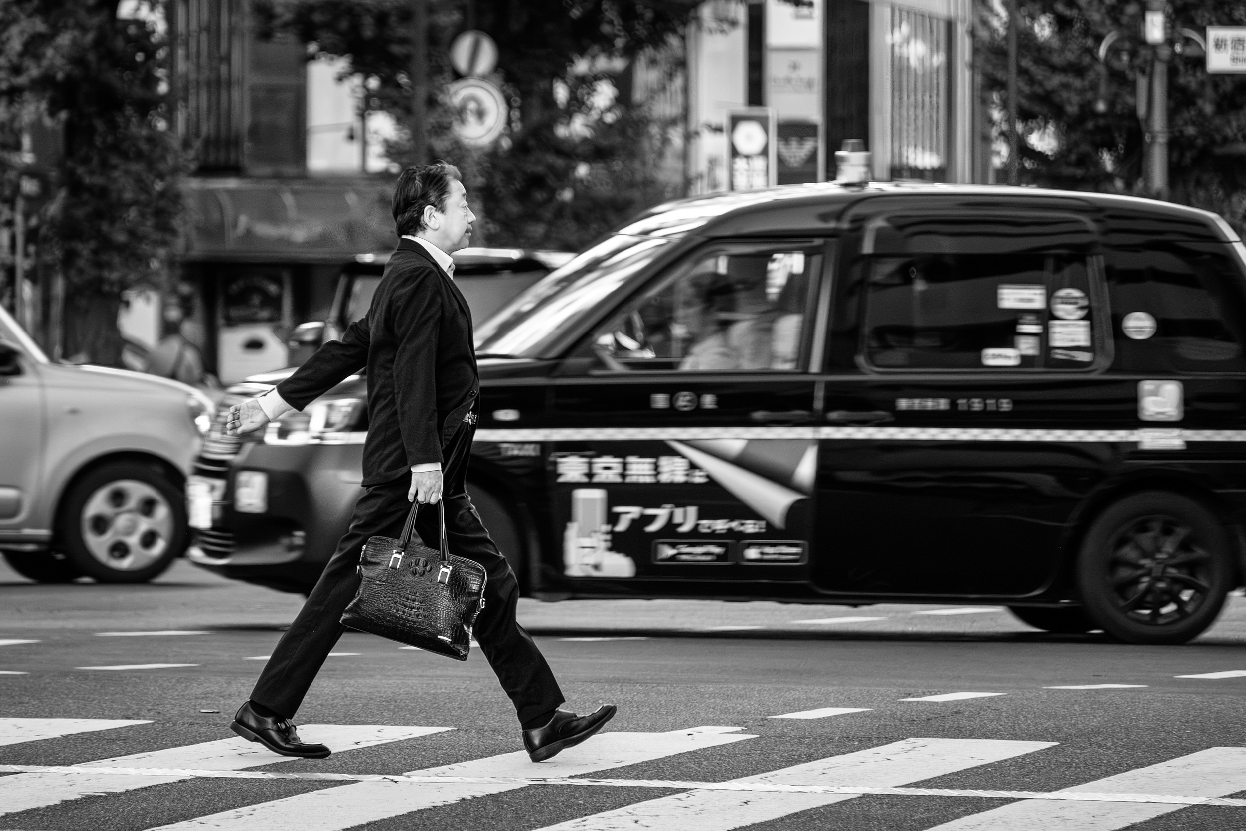 Black and white street photograph of a businessman mid-stride crossing the road near a taxi.