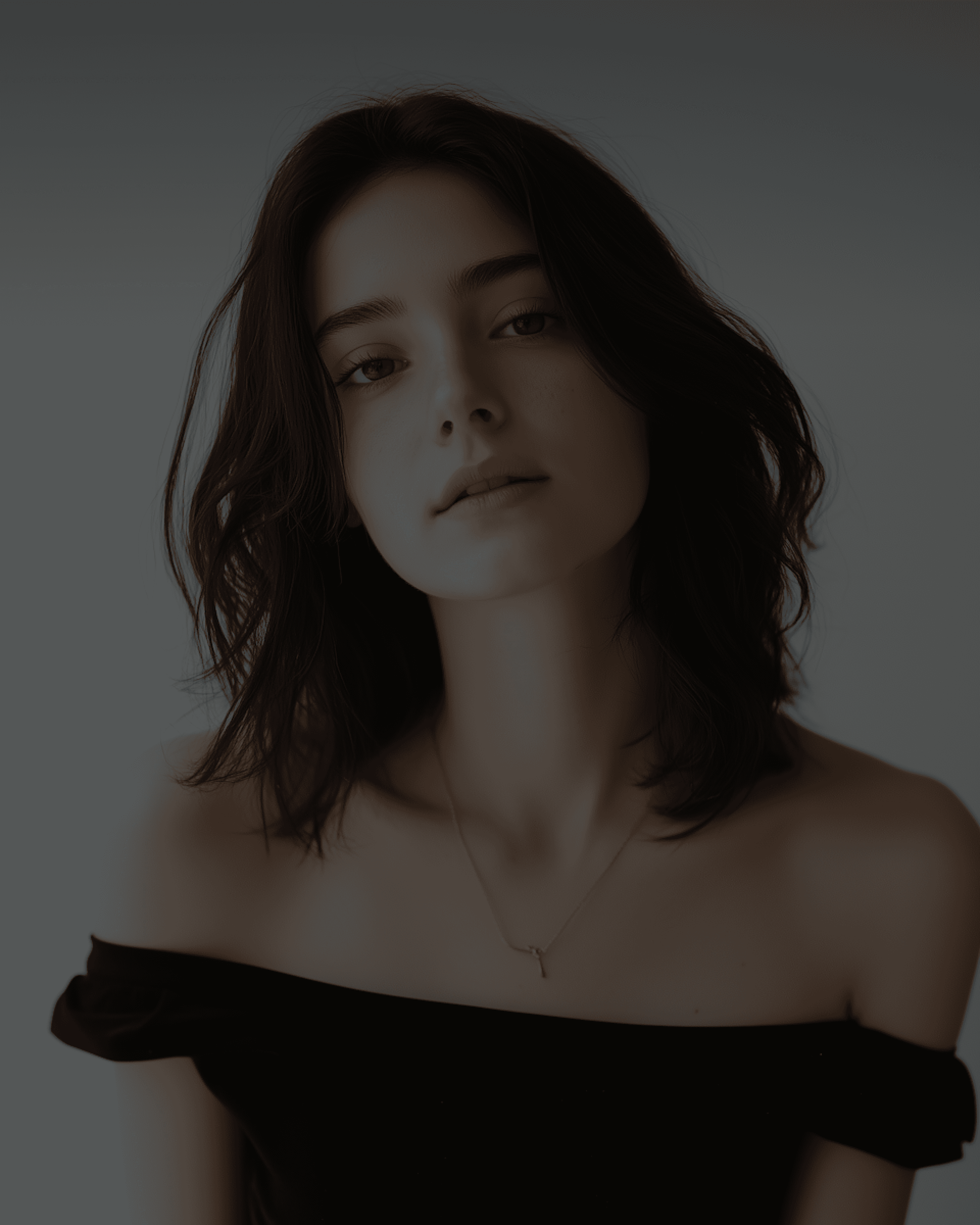 Portrait of a young woman with shoulder-length dark hair, wearing a black off-the-shoulder top.