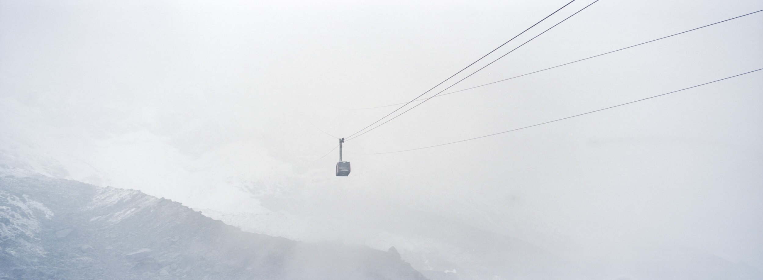 A Gondola disappearing in the clouds with mountain tops slightly peaking through the clouds shot on a Hasselblad XPan