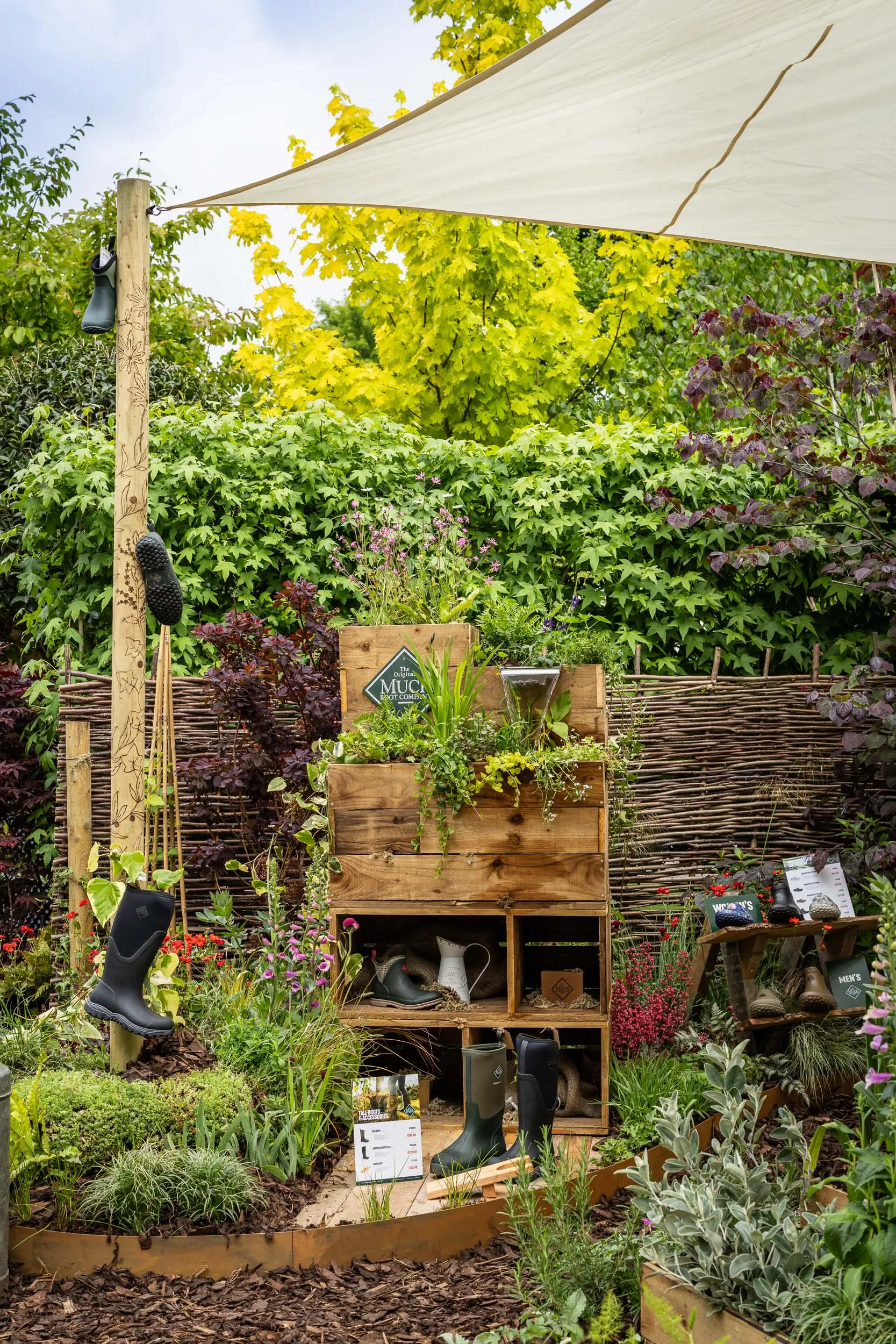 A lush garden with green plants, wooden shelves, and a shelter above, creating a serene natural space.