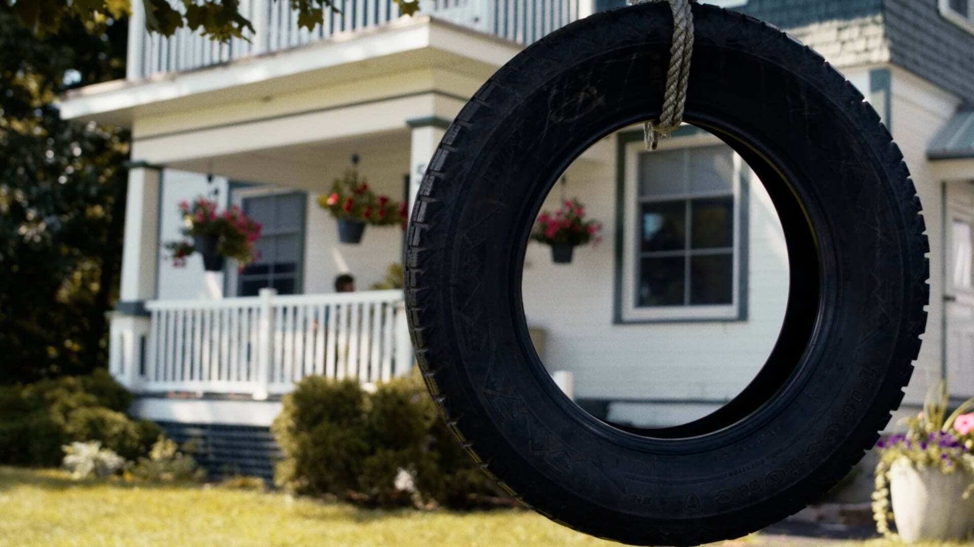 A tire swing hanging in front of a suburban house with a well-kept lawn