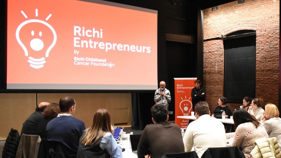 People attend a presentation for "Richi Entrepreneurs" by Richi Childhood Cancer Foundation. A speaker stands by a screen.