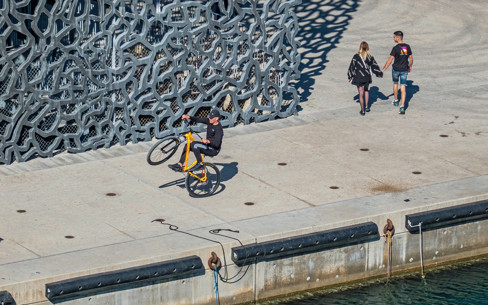Fietser die een wheelie maakt bij de unieke gevel van het Mucem in Marseille.