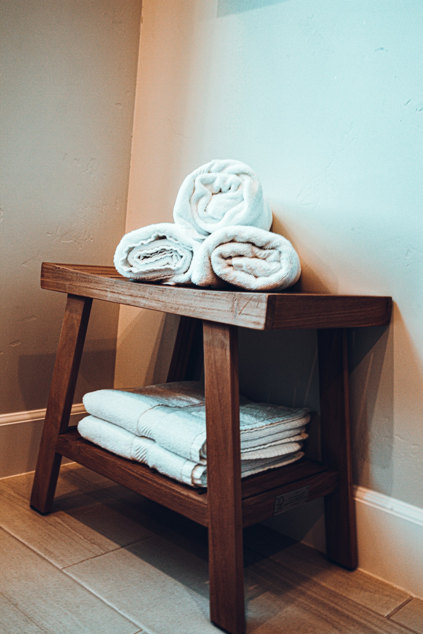 Rolled white towels on a wooden bench against a warm plaster wall