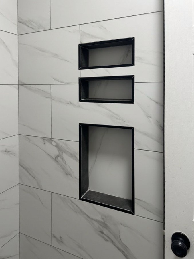 Custom shower wall with large format white marble-look tiles and three built-in rectangular shower niches with contrasting black trim.