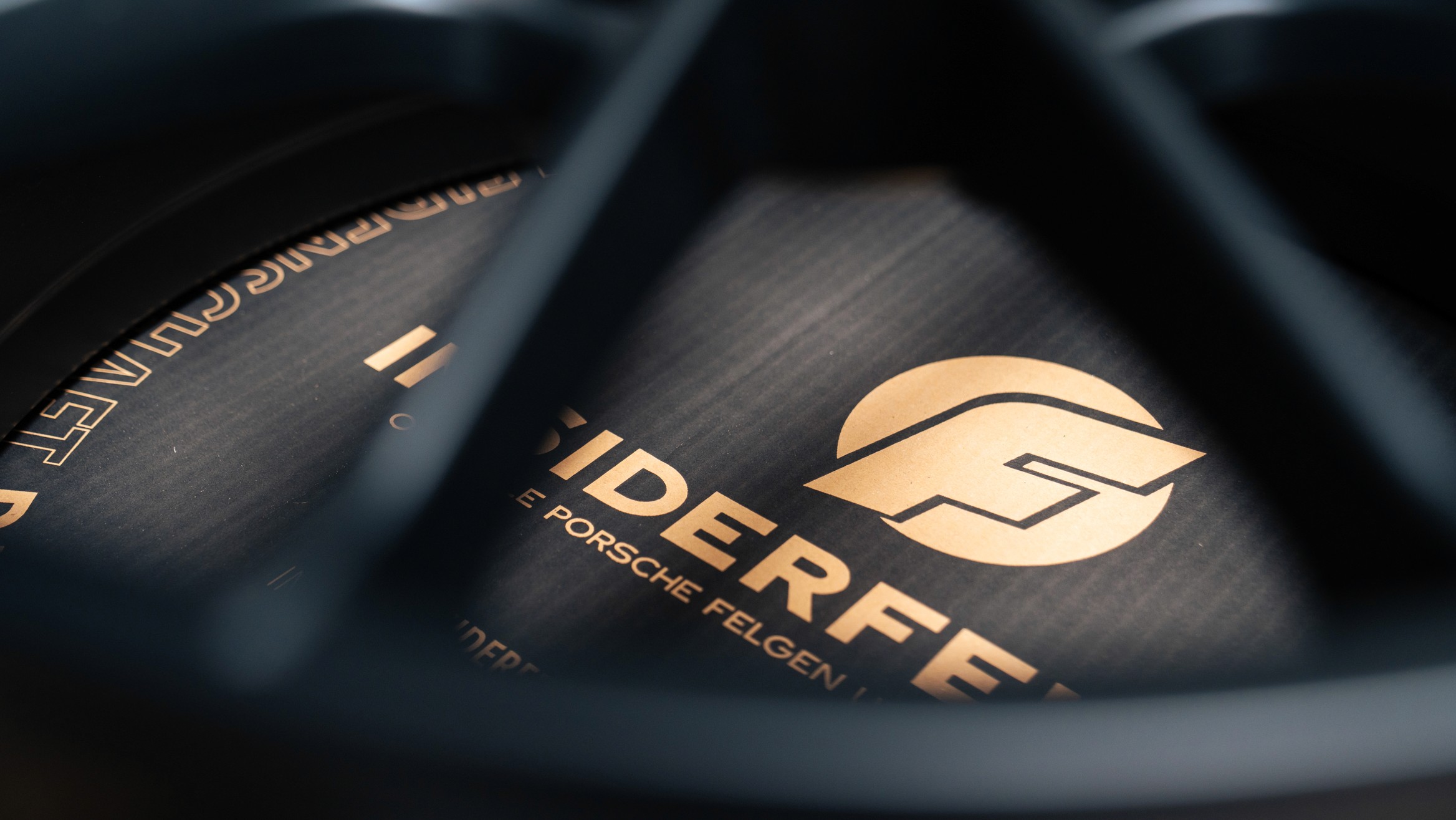 Detailaufnahme einer Porsche-Felge mit Fokus auf die edle Insiderfelgen-Radverpackung – stilvoll inszeniertes Logo und Claim „Originale Porsche Felgen“ in goldener Schrift.