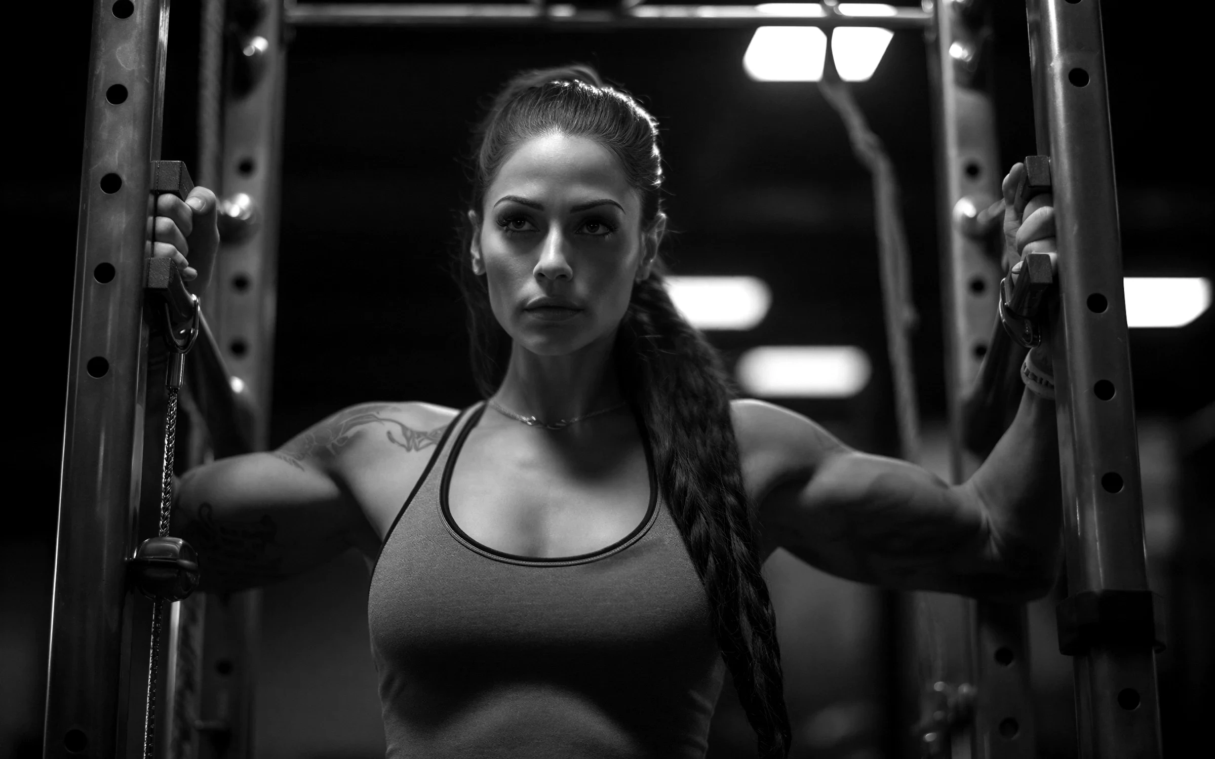 Woman gripping the handles of a power rack in a dark gym