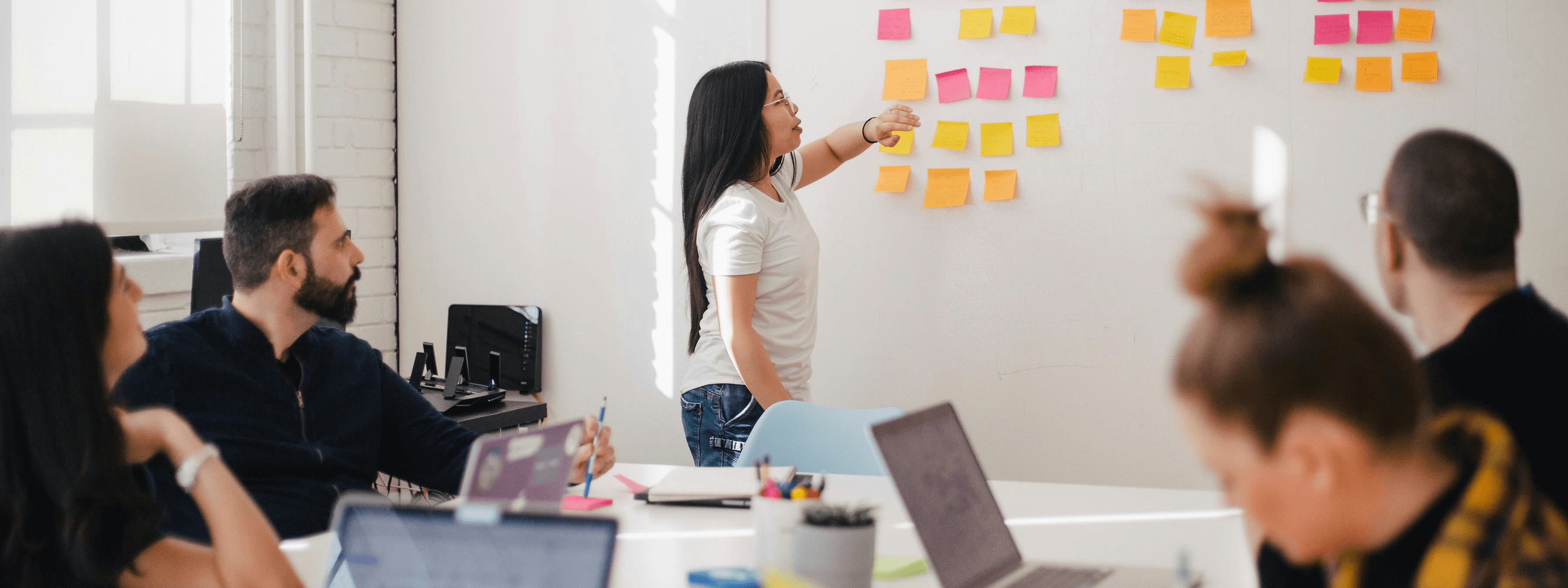 Photo of a woman presenting post it notes in a large meeting room. Photo by Jason Goodman.