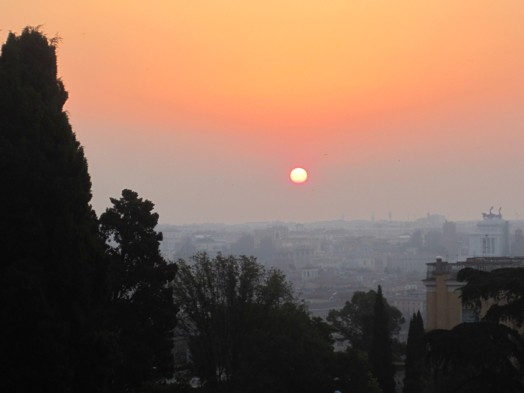 A photo of the sun rising or setting above the city scape.