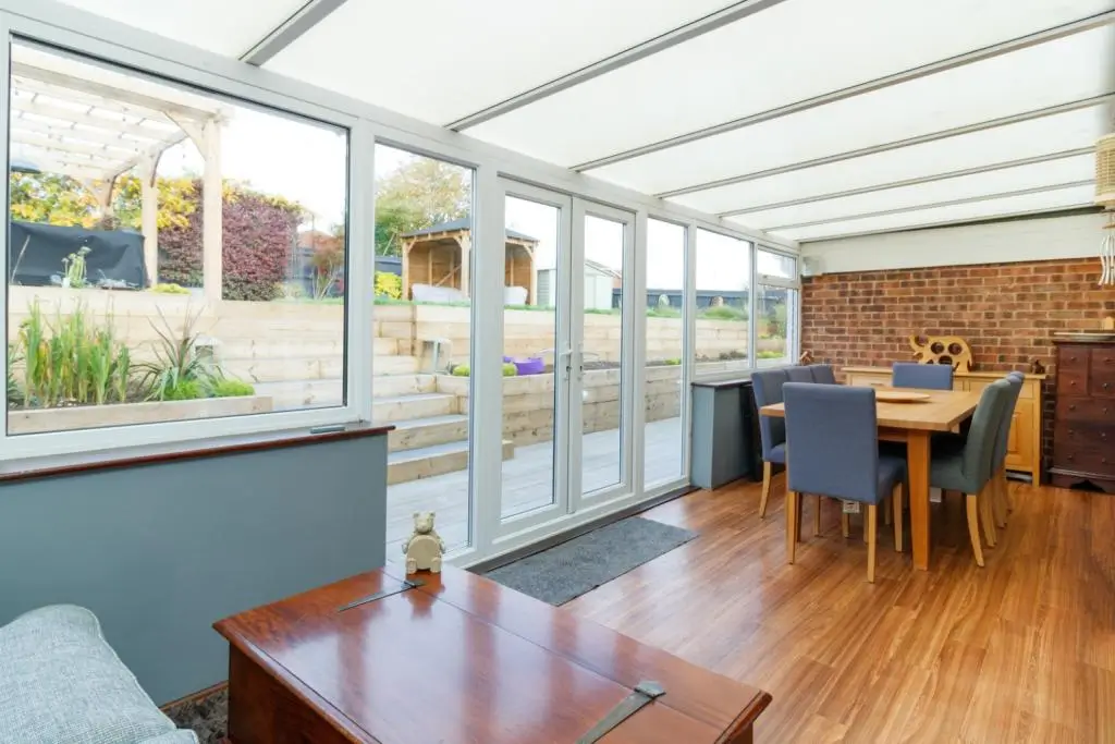 Bright modern room with large windows, wooden floor, and a dining table in a cozy interior setting.