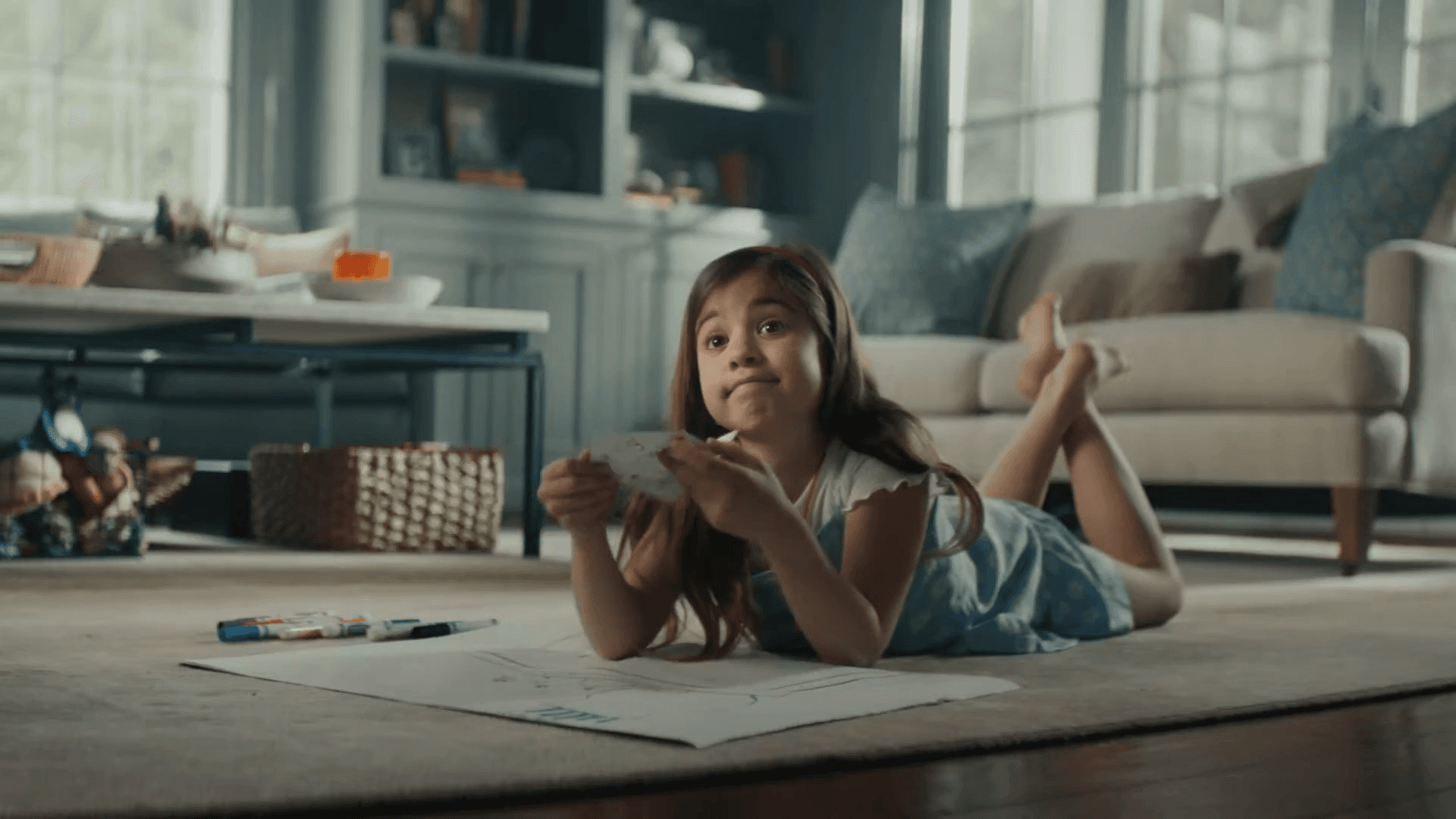 A child lies on a carpet, drawing contentedly with crayons in a cozy, well-lit living room.