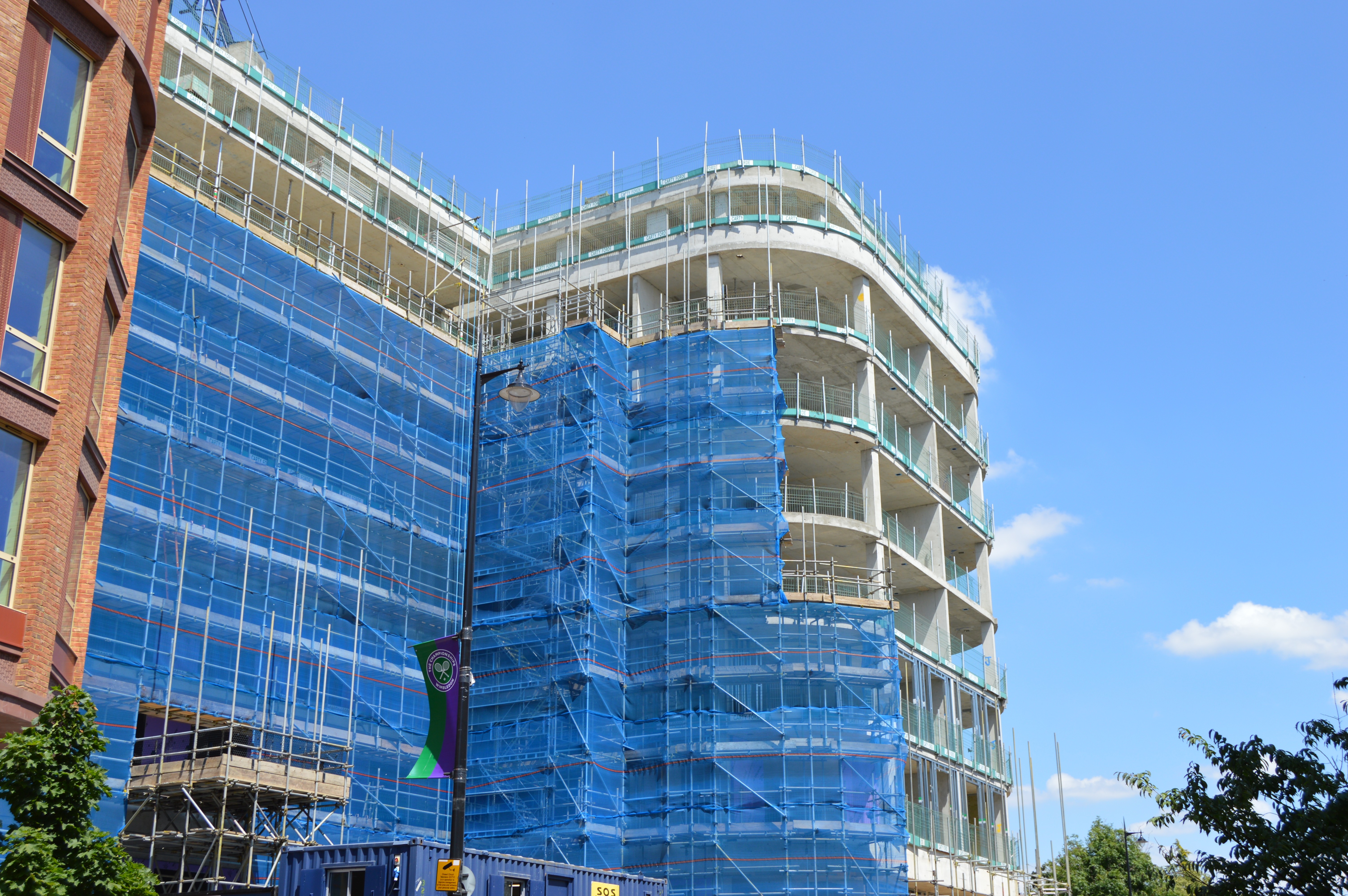 A building under construction wrapped in blue scaffolding wrap.