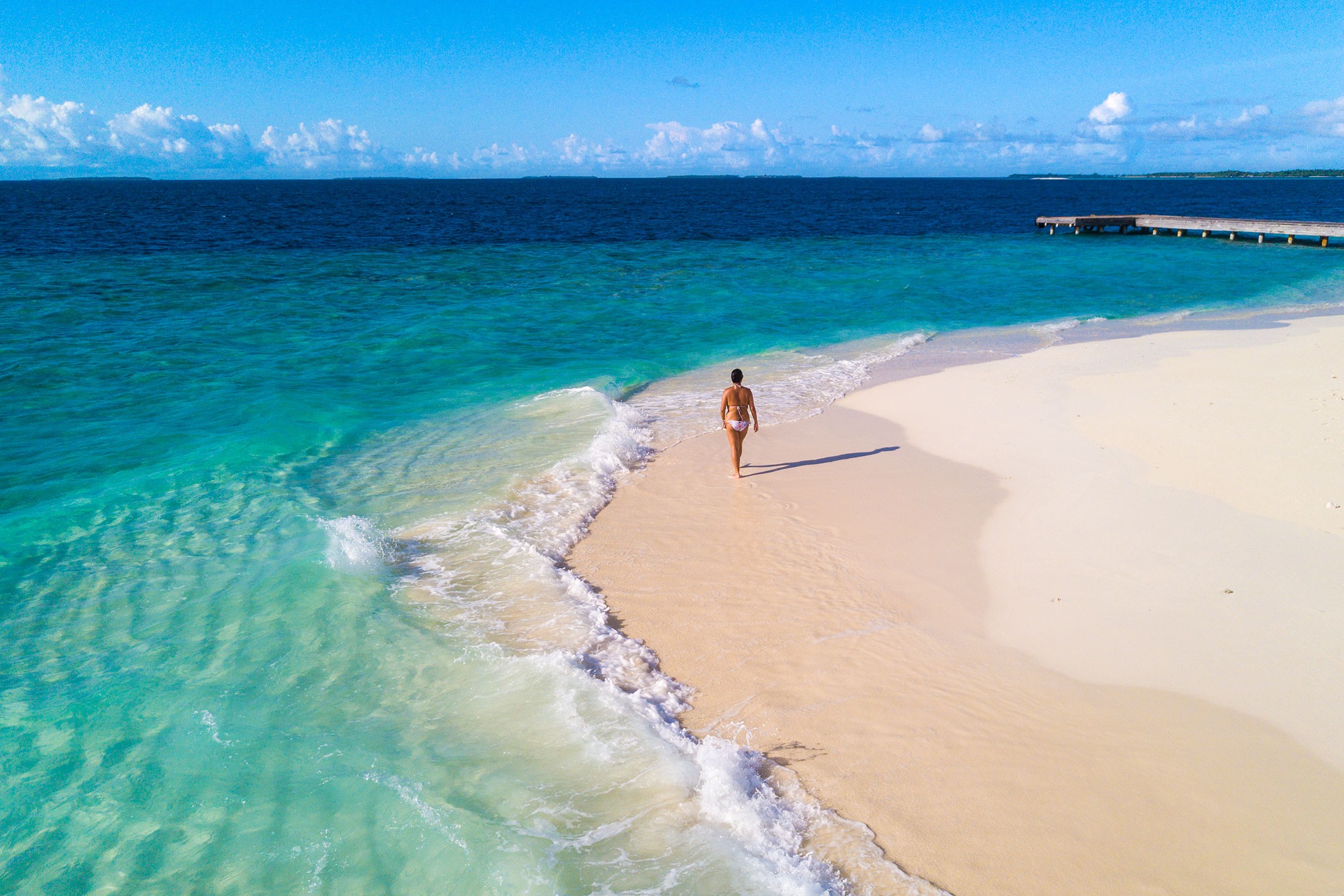 Golden sand meets turquoise waves under bright sunlight at a serene tropical beach paradise.
