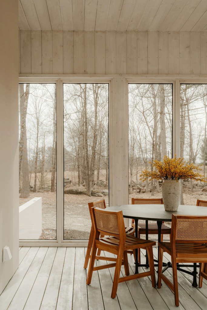Dining table with chairs by large windows overlooking trees