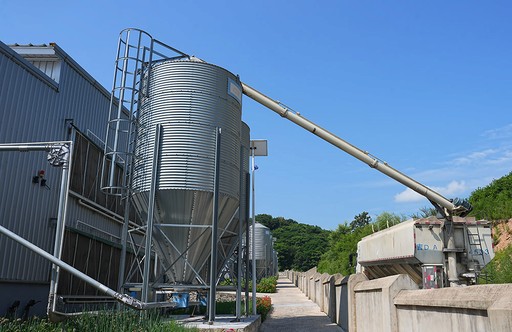 Large corrugated metal silos with an inclined conveyor belt, representing the robust infrastructure for processing egg.