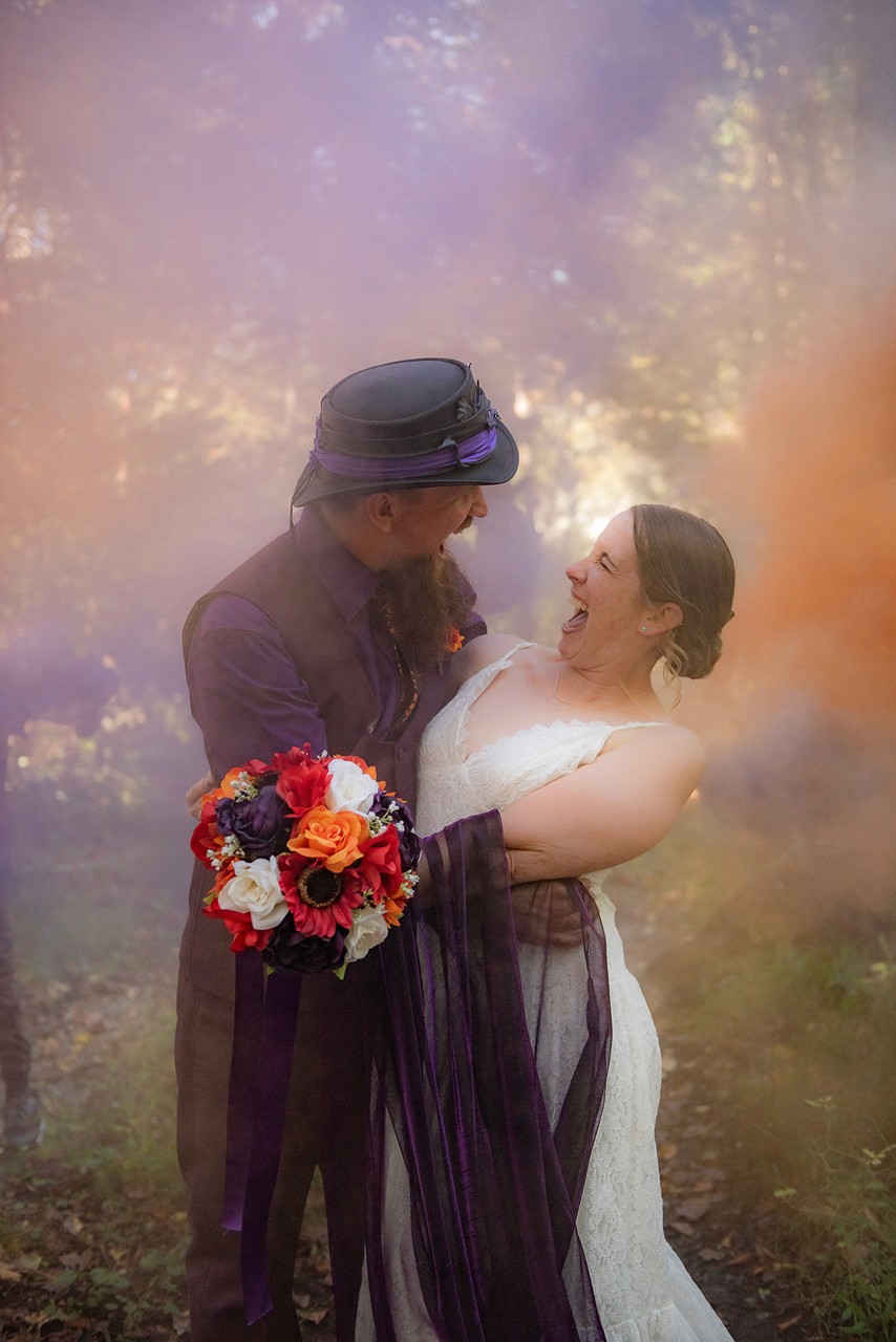 Happy couple celebrating wedding in smoky forest with colorful smoke bomb effects