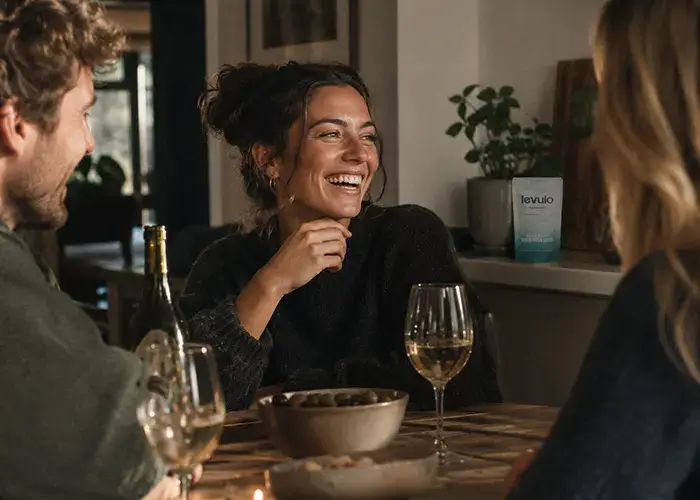 3 friends having dinner drinking wine with a Levulo Foundation pouch in the background