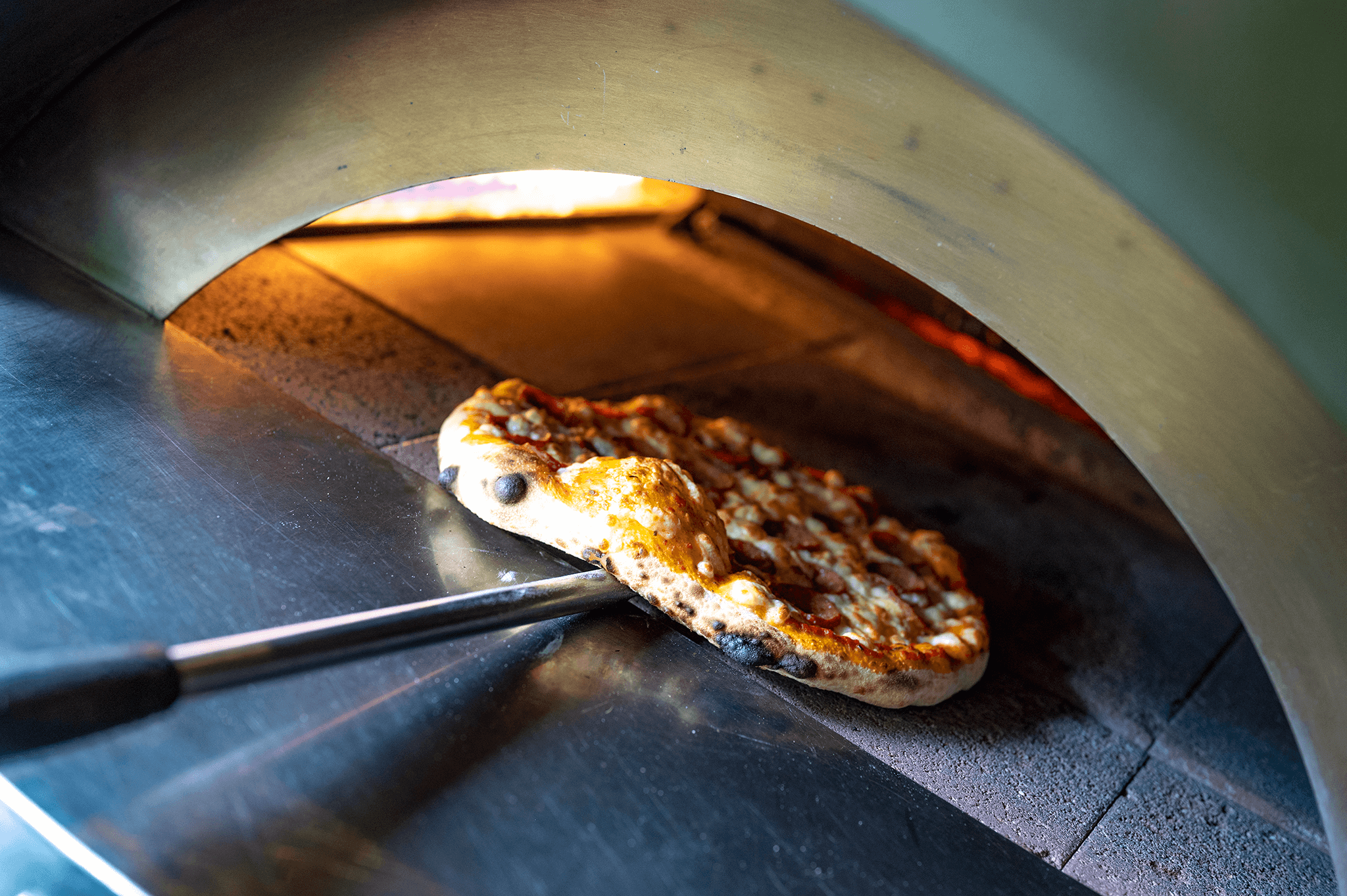 A freshly made pizza baking in a wood-fired oven, with bubbling cheese and golden crust.