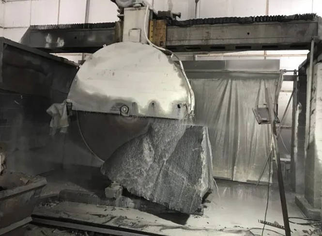 The Dinosaw Bridge Single-Blade Cutting Machine in operation, demonstrating its powerful blade cutting through a large stone block with ease, showcasing the machine's efficiency and cutting capability.