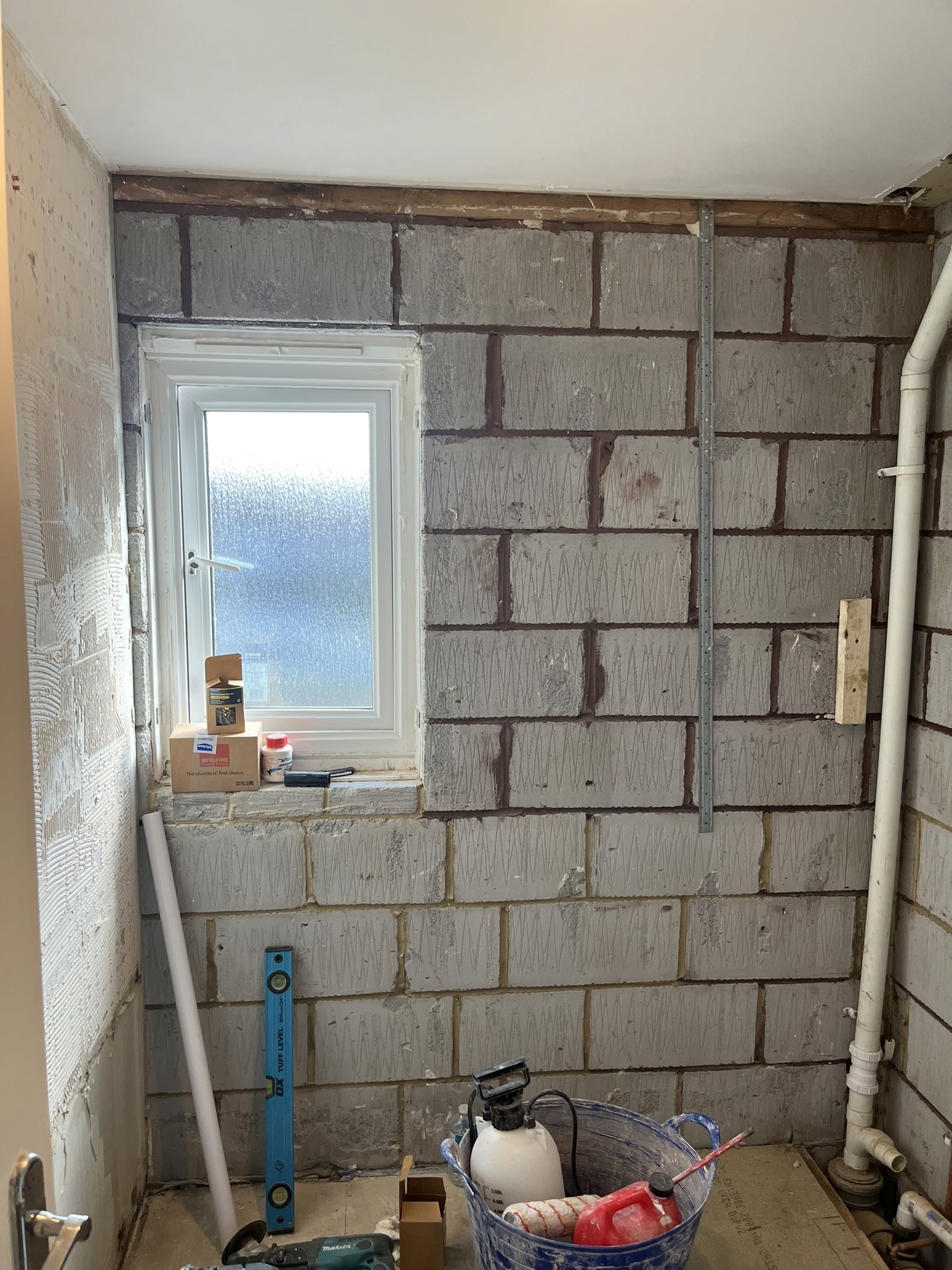 Bathroom under construction, with exposed blockwork, plumbing and a frosted window.