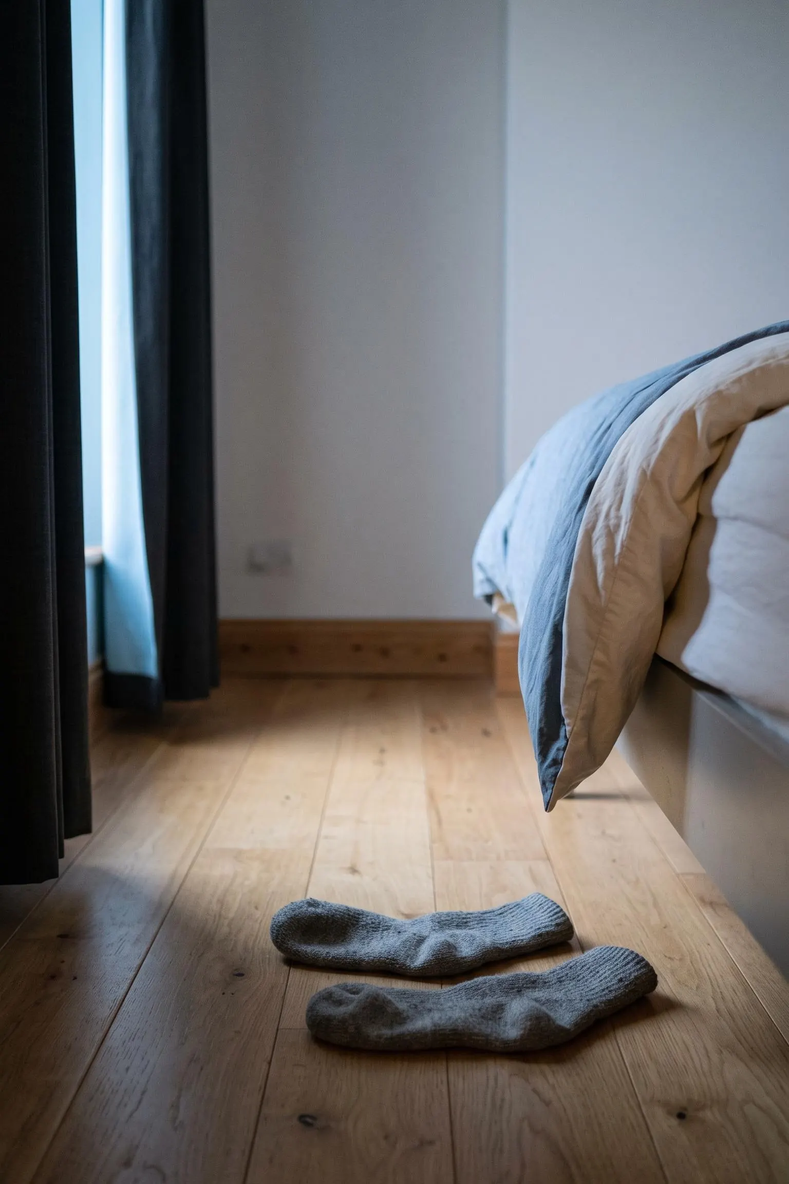 Woollen socks on bedroom floorboards at first light, the foot of a bed beyond