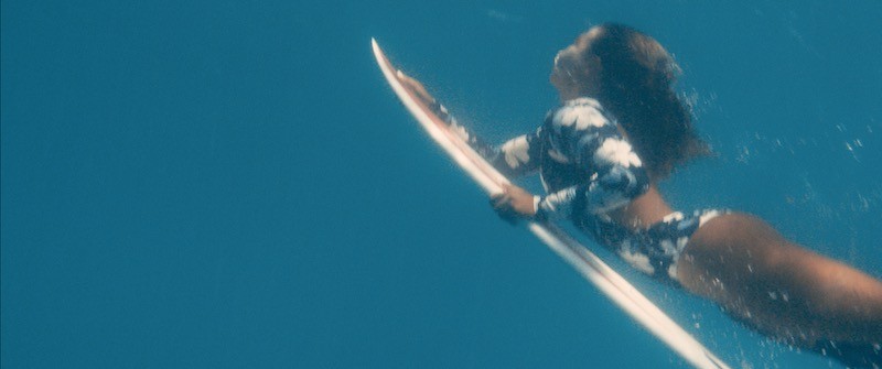 Surfer duckdiving in the ocean holding on to her board