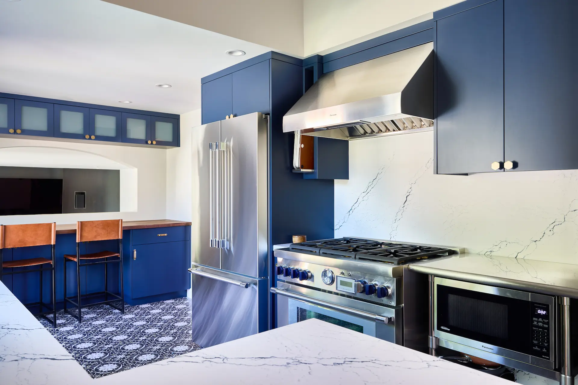 Wide angle view of the kitchen showcasing the high-end Thermador appliances, integrated seamlessly within the blue flat-panel cabinets with antique brass hardware, exemplifying modern transitional style in the Huntington Beach Kitchen. Photo by Todd Huge.