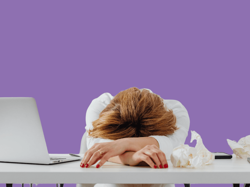 View os woman exhausted at her desk with her head down experiencing an EBV flare up