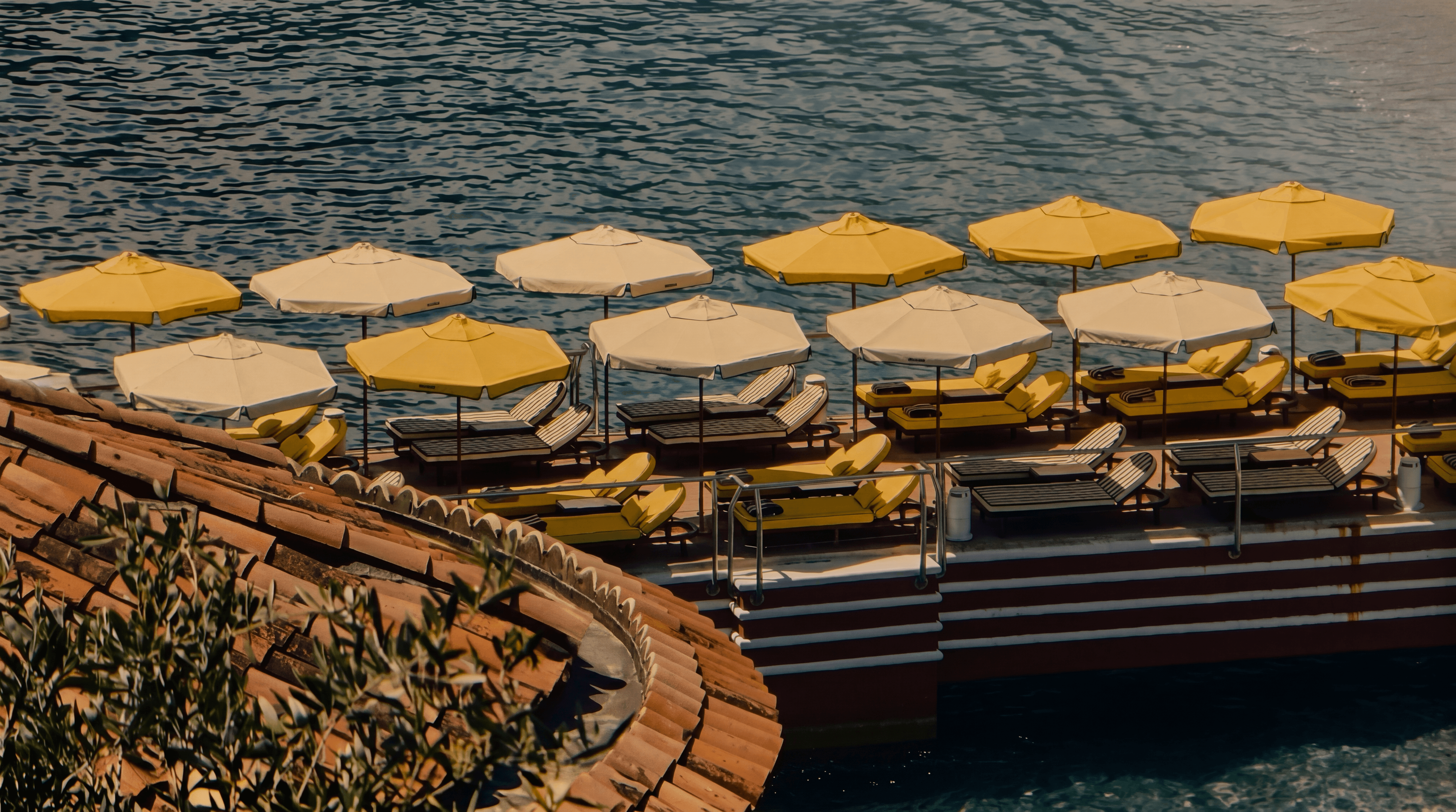 Waterfront bathing deck with yellow parasols viewed over terracotta rooftops, Monte Carlo Beach, South of France — curated by VELUMA Private Residences