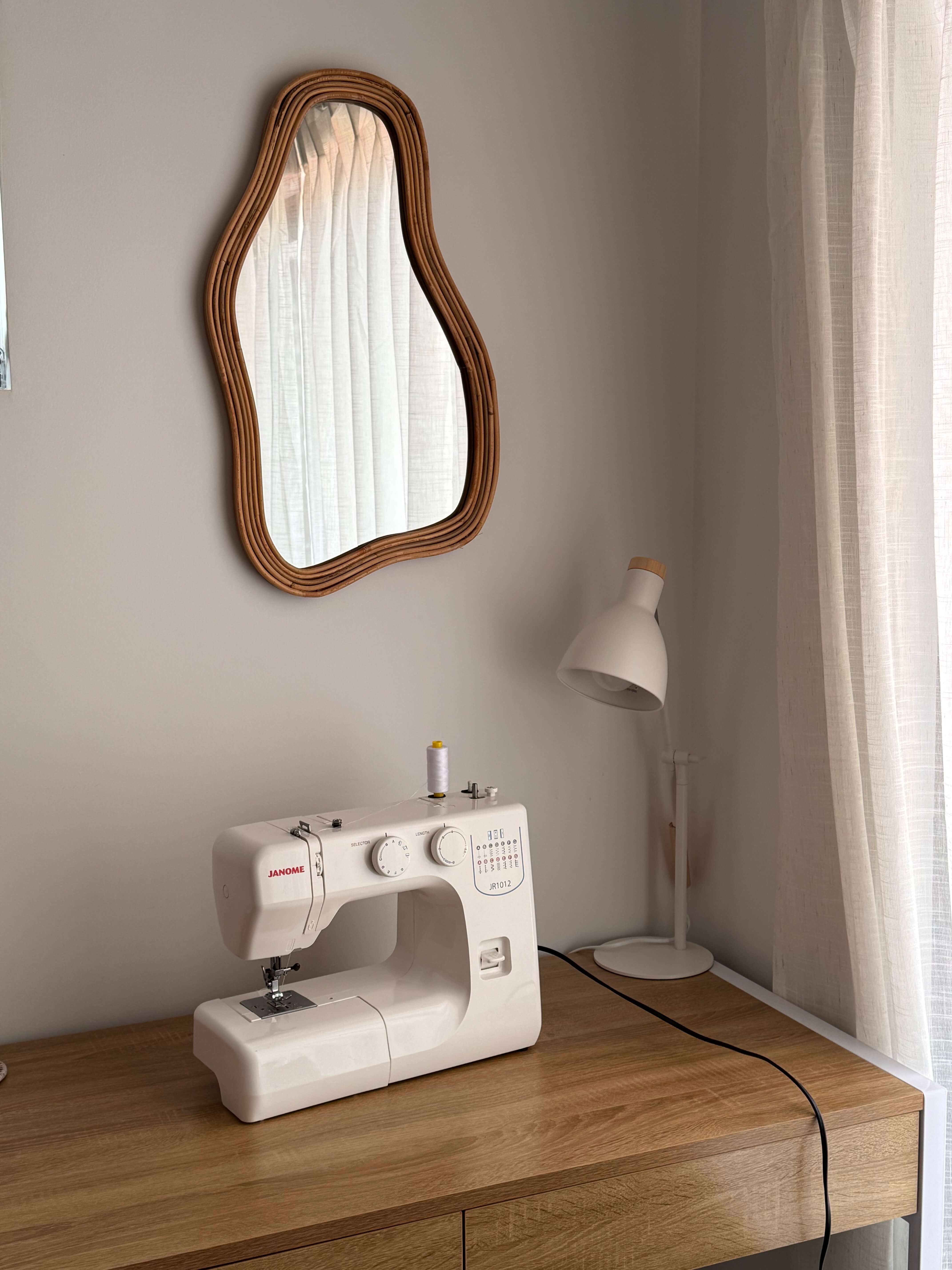 A sewing machine set on a wooden desk with a lamp and blob shaped mirror