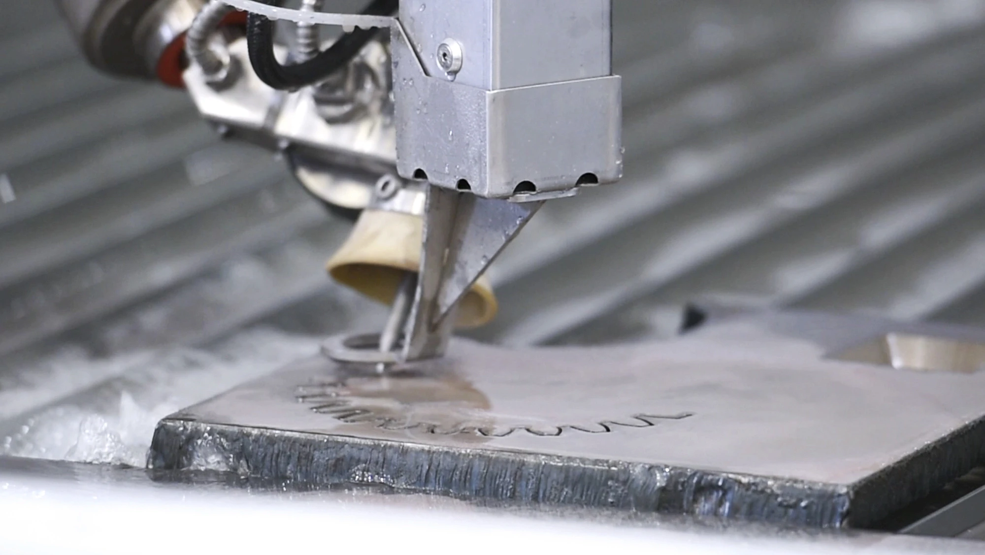 Close-up of a waterjet cutter slicing a sheet of metal, with water and spray around the cutting nozzle.