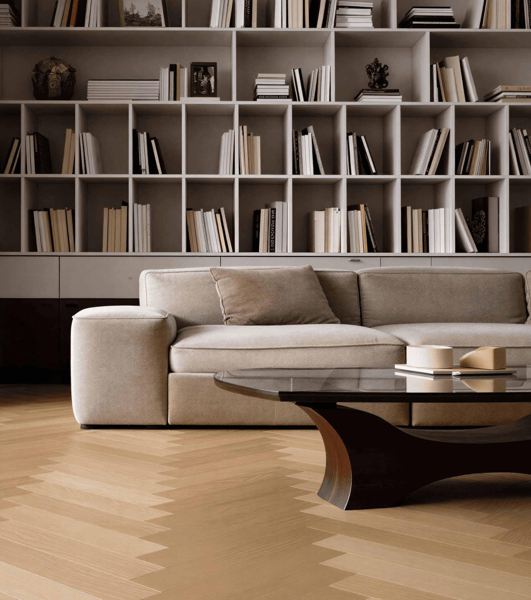 A cozy living room features a soft beige couch adorned with plush cushions, set in front of a modern, dark wood coffee table with a glass top, all against a backdrop of a stylish floor-to-ceiling bookshelf filled with neatly arranged books, providing a warm and sophisticated atmosphere.