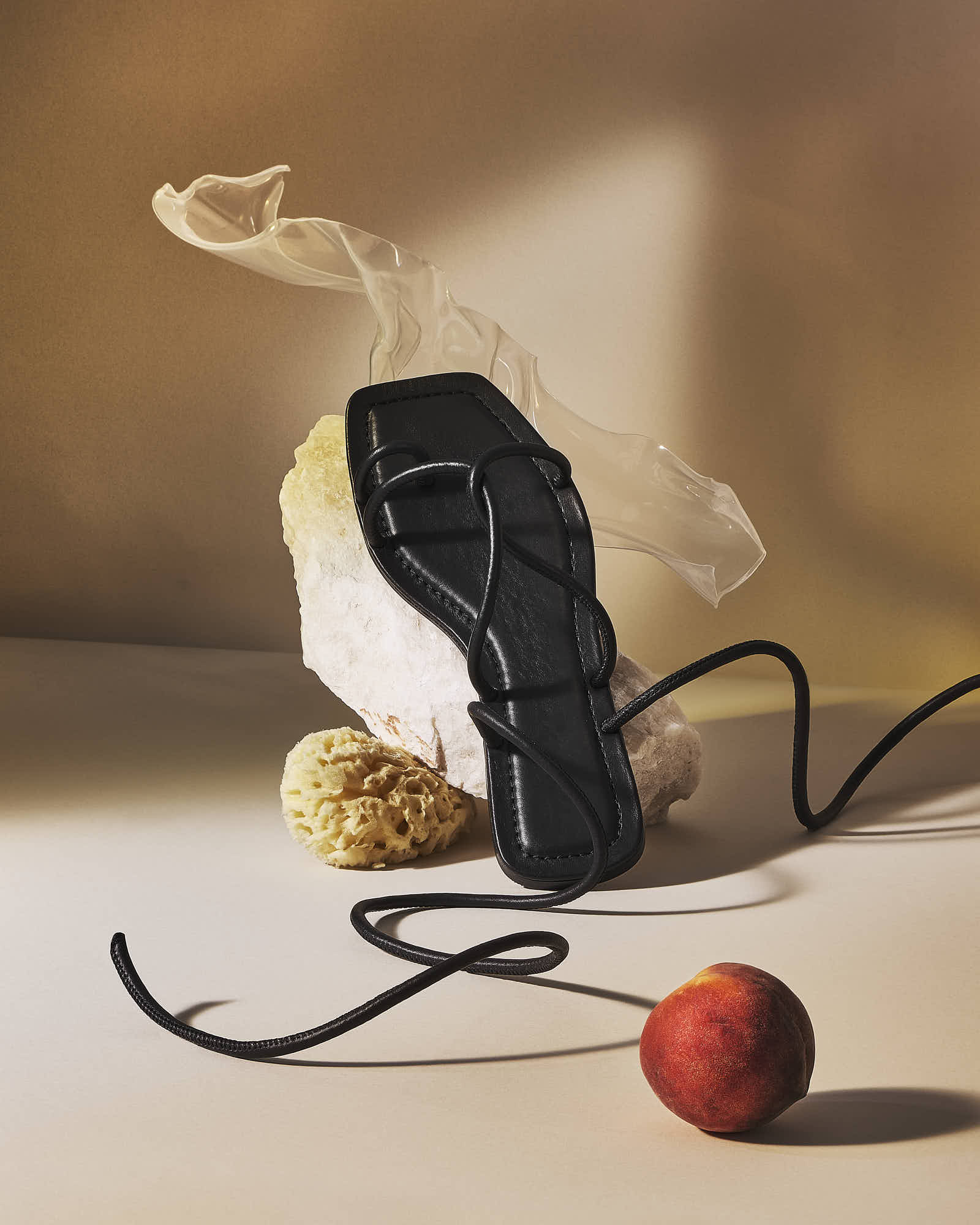 Elegant black sandal with laces beside a peach and decorative elements on beige backdrop.