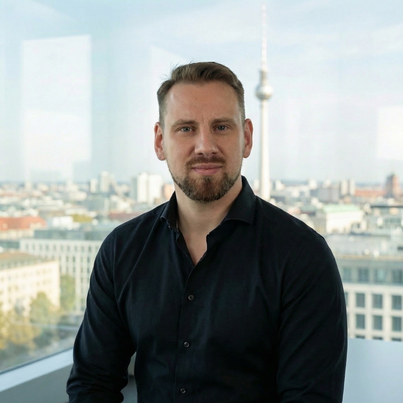 A woman with short curly hair wearing a black t-shirt looks into the camera.