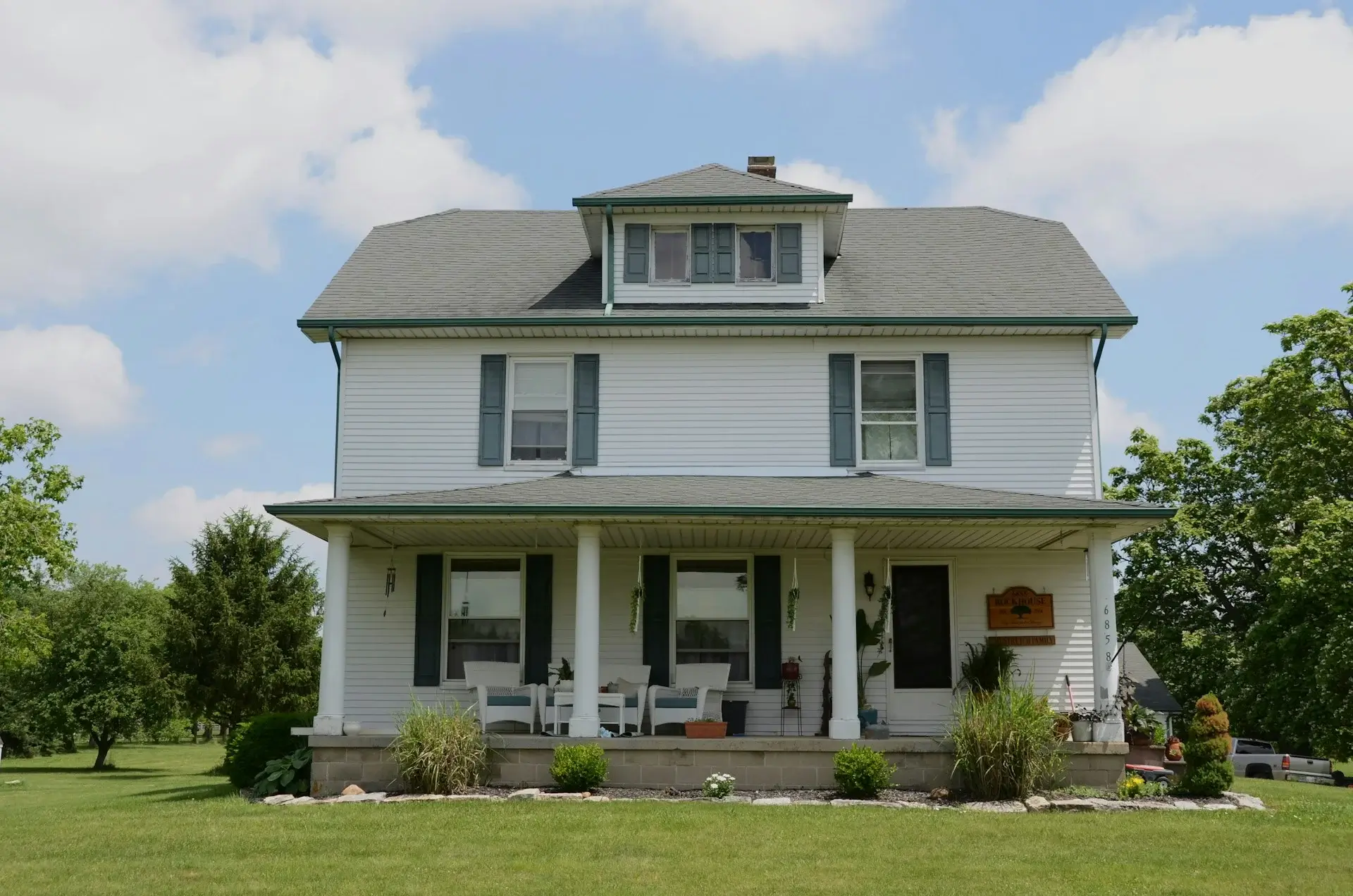 Traditional white farmhouse with a front porch, columns, and an open green yard.