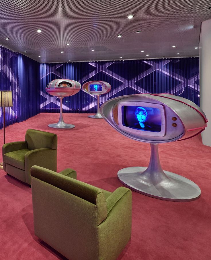 Retro futuristic lounge with egg shaped screens on pedestals and green armchairs