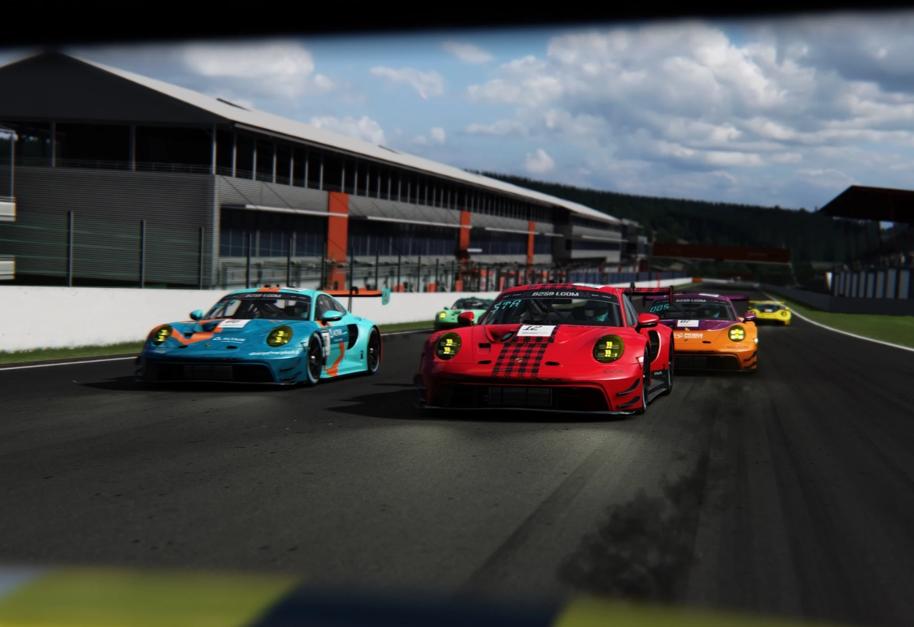 Group of colorful racing cars competing on a track, led by a red car with black racing stripes under a partly cloudy sky.