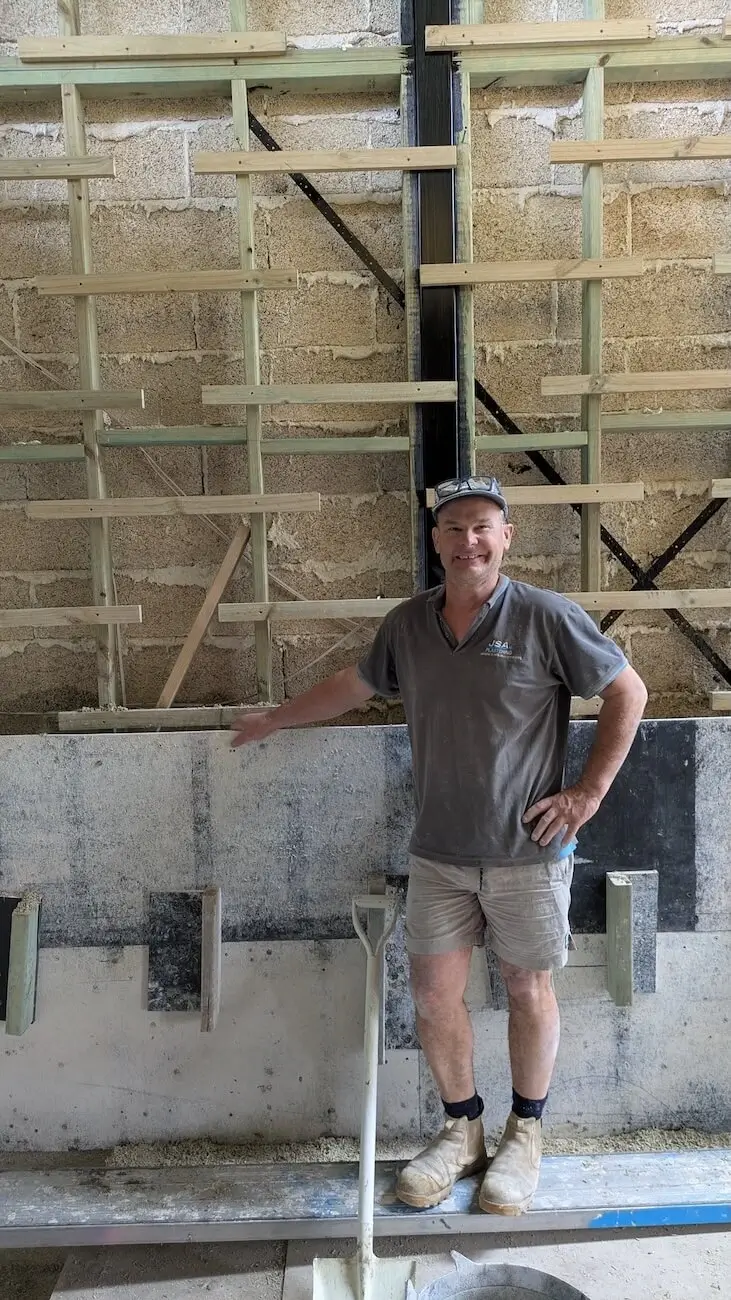building a beautiful Hempcrete house, Jamie has managed to achieve very high energy performance. In this picture, you can see Jamie standing in front of a Hempcrete block wall and smiling at the camera