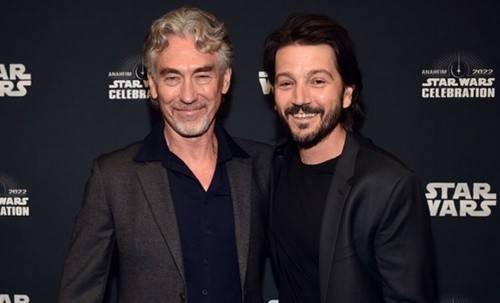 Tony Gilroy and Diego Luna smiling in front of a pose wall at Star Wars celebration