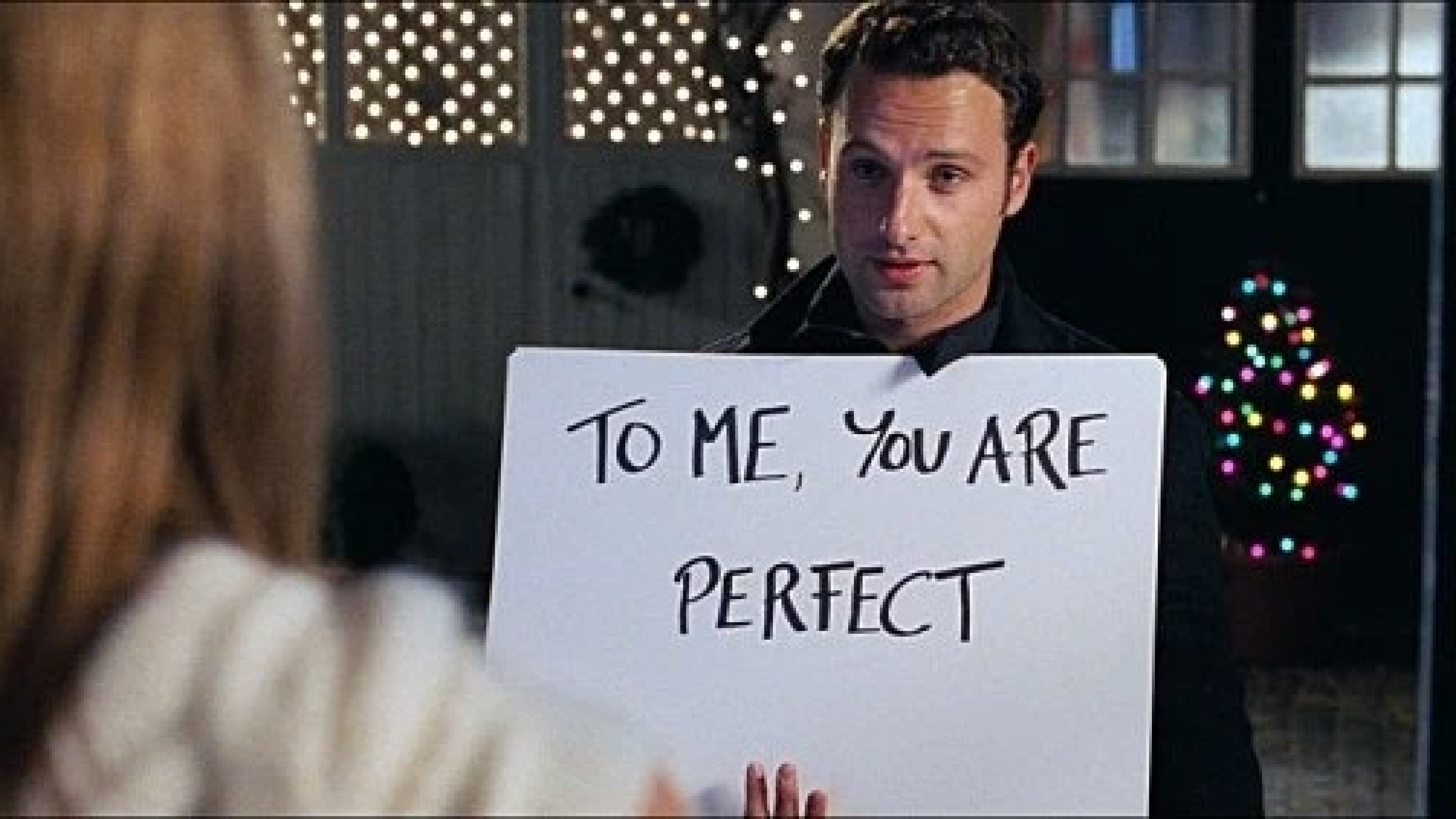 영화 러브 액츄얼리의 카드 고백 장면. 한 남자가 'To me, you are perfect'라고 적힌 흰 카드를 들고 서 있다.