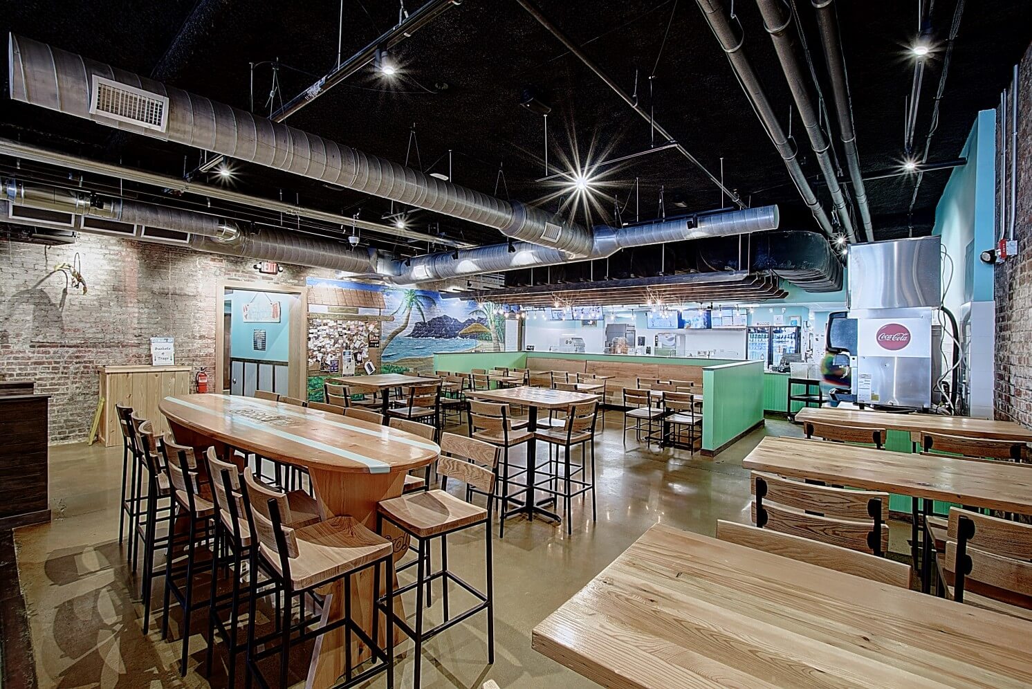 A modern restaurant interior with wooden tables, chairs, and bright lighting, featuring an open layout.