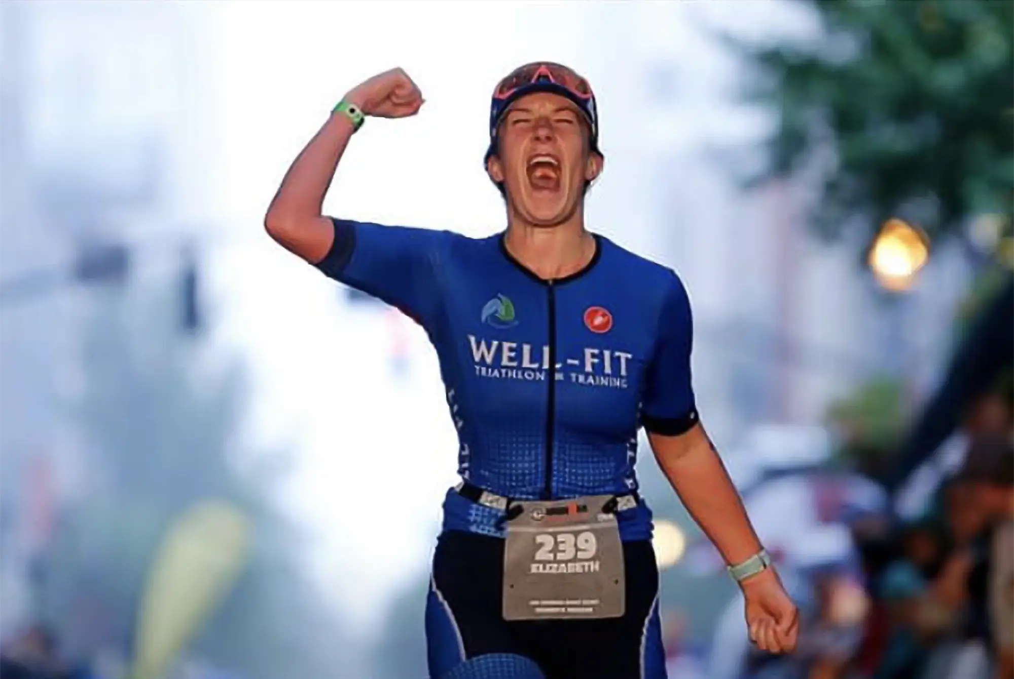 Well-Fit athlete Liz crossing the Ironman finish line with fist raised, placing 14th at the Ironman World Championship