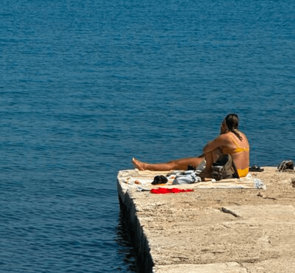 woman in a yellow bikini sitting on a stone pier in front of the sea